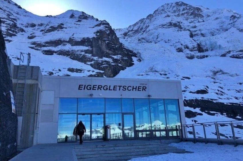 A building named 'Eigerletscher' with a glass facade, set against a snowy mountain backdrop. 3