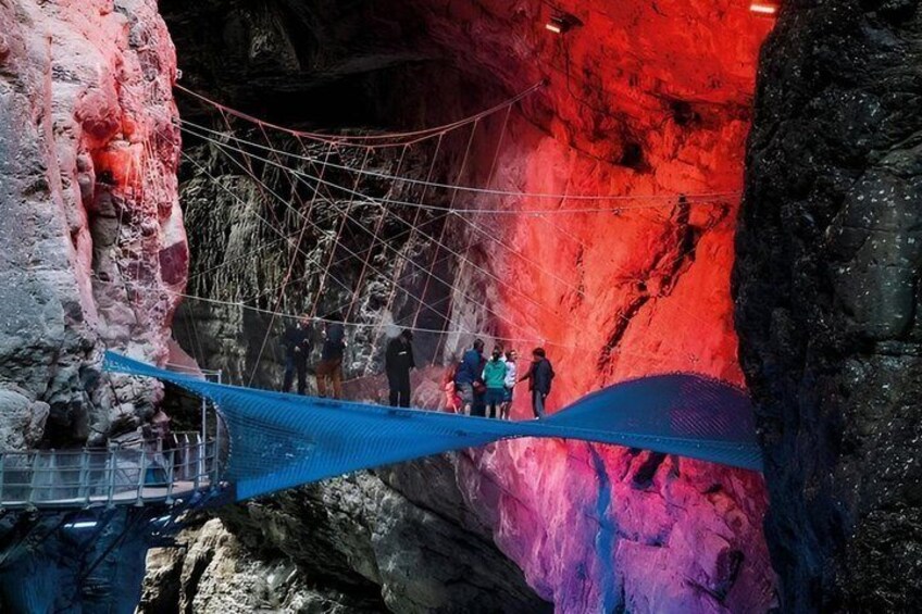 A rope bridge over a cave with red walls and people walking on it. 1