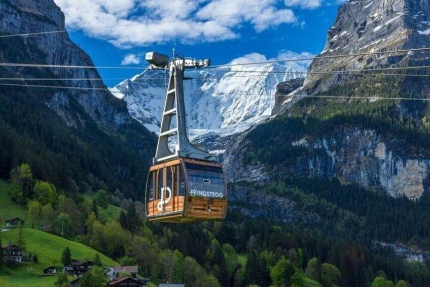 A cable car with 'Pingslegg' written on it, suspended over a mountainous landscape with snow-capped peaks and green valleys. 5