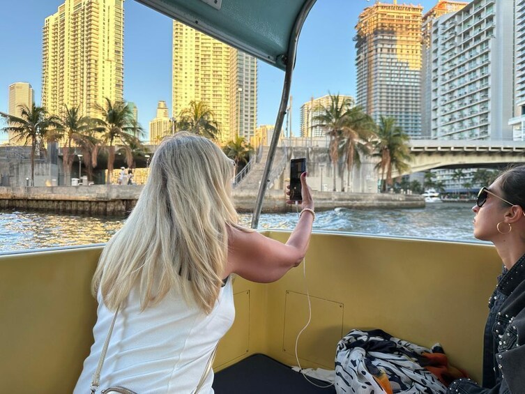 Une personne prend une photo avec un téléphone intelligent, avec un bateau, une rivière et de grands bâtiments en arrière-plan. 2