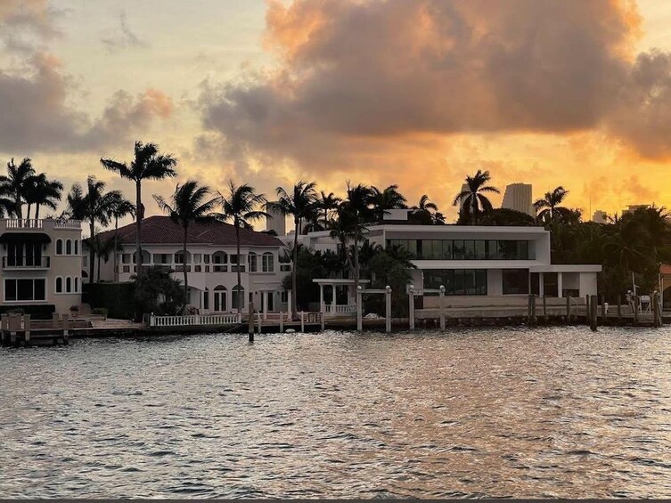 Une propriété située au bord de l’eau, dotée d’une architecture moderne, de palmiers et offrant une vue sur un ciel au coucher du soleil. 1
