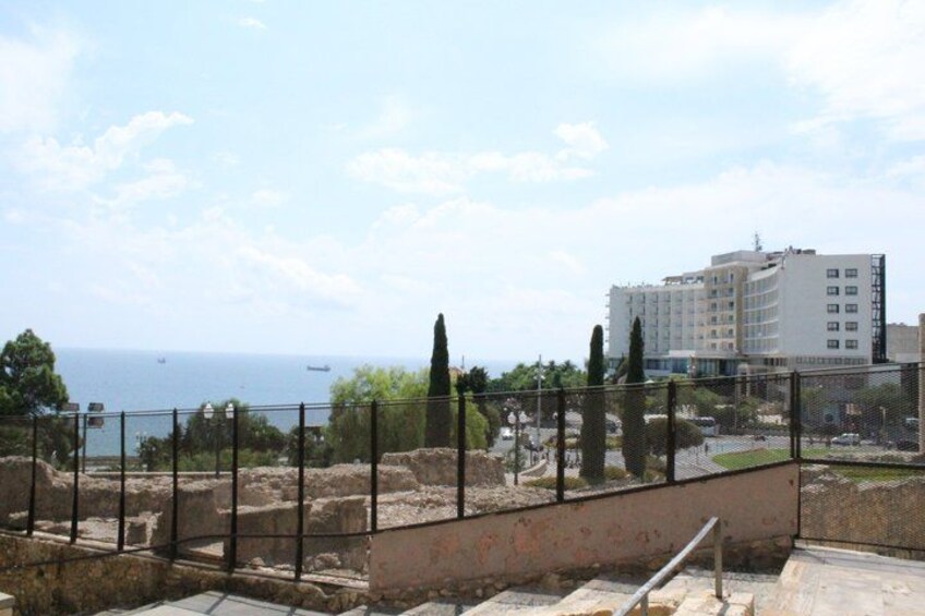 A coastal archaeological site with ancient ruins, a modern building, and a clear view of the sea. 4