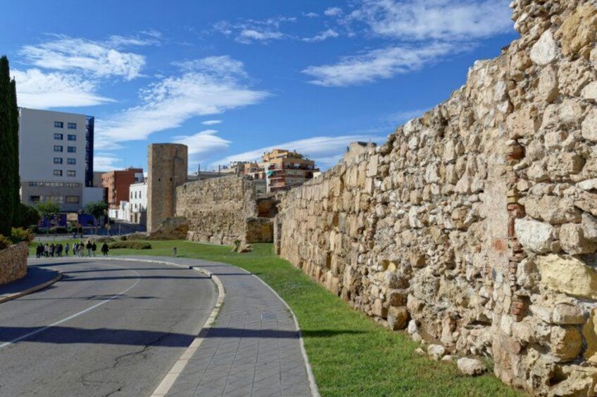 A stone wall, a curved road, and modern buildings in the background. 5