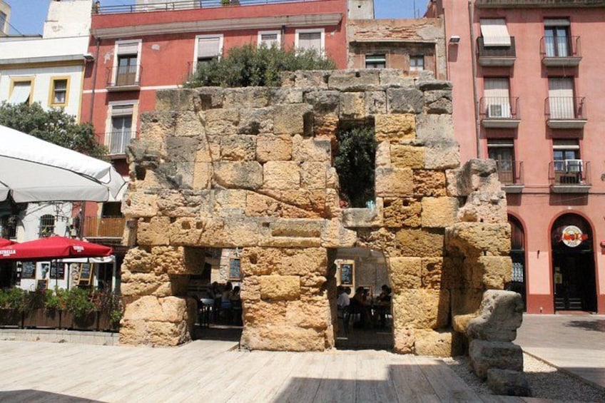 A stone ruin with a doorway, surrounded by modern buildings. 5