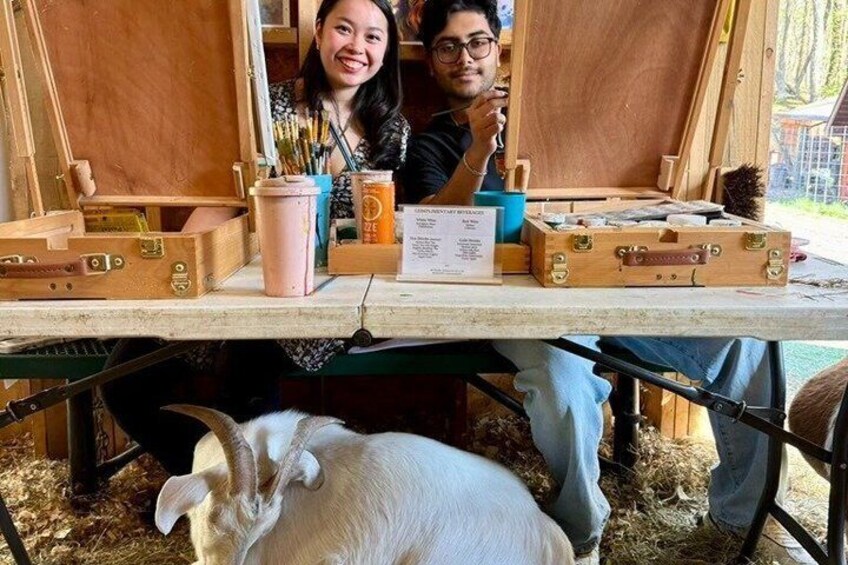 A person painting a wooden easel, a pink cup, and a white goat on a table. 5