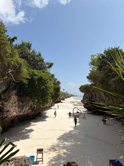 A beach with people walking, a heart-shaped structure, and tropical vegetation. 4