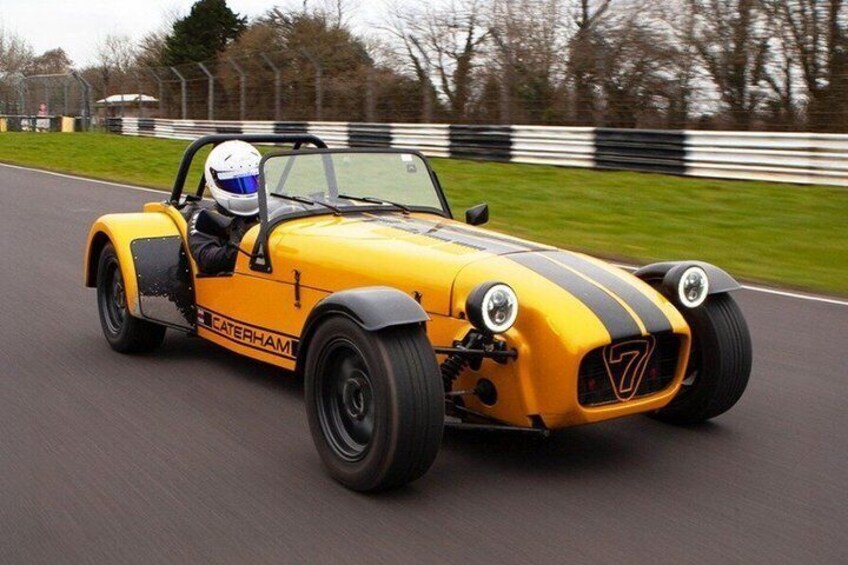 A yellow sports car with racing stripes on a racetrack. 1