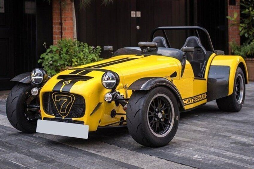 A yellow sports car with black racing stripes parked on a paved surface. 5