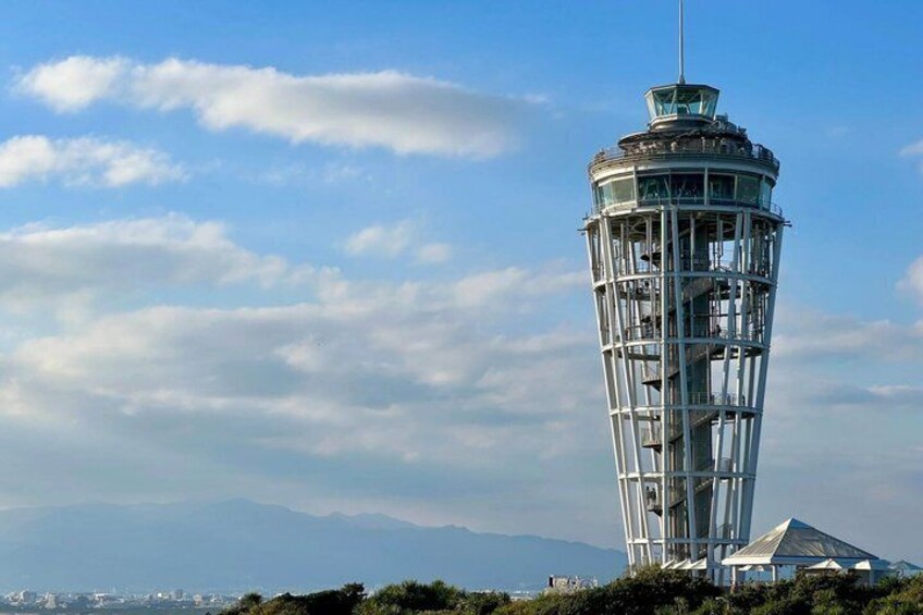 A tall, cylindrical tower with a glass enclosure, surrounded by a clear sky and distant mountains. 2
