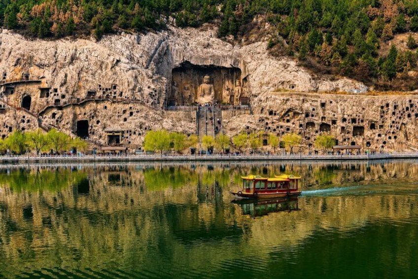 A rocky cliff with ancient rock-cut dwellings and a boat on a calm lake. 2