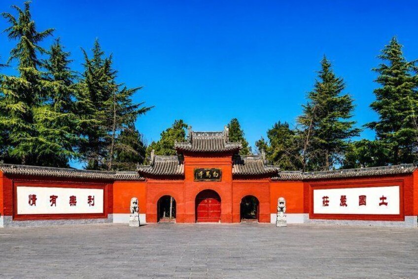 A traditional Chinese gate with red walls and a tiled roof, flanked by two statues, set against a backdrop of trees and clear blue sky. 4