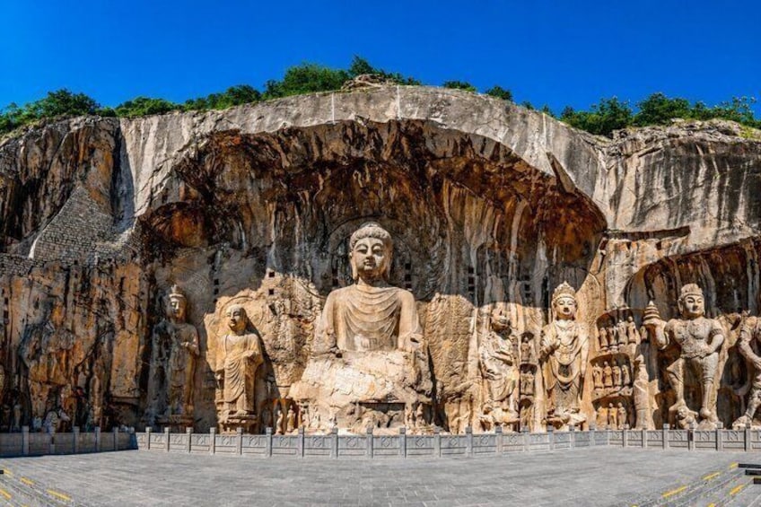 Large Buddha statues carved into a cliff face, with a clear sky above. 1