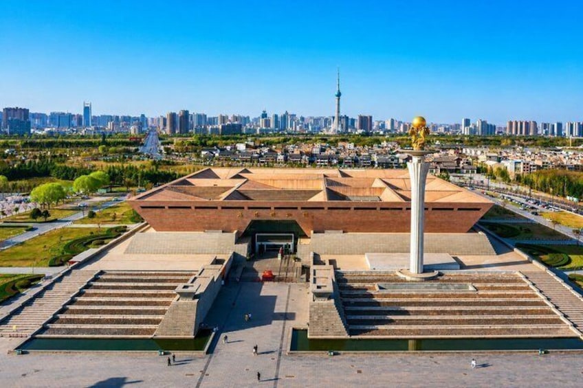 A large, modern building with a unique roof design, surrounded by a well-maintained park and a city skyline in the background. 3