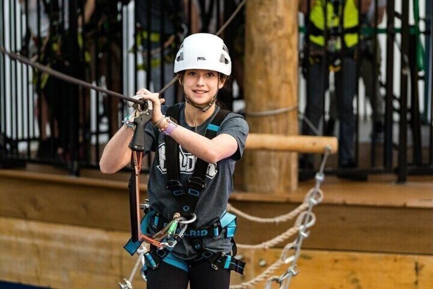 A person engaged in a zip-lining activity, wearing a helmet and harness, with safety equipment and ropes visible. 5