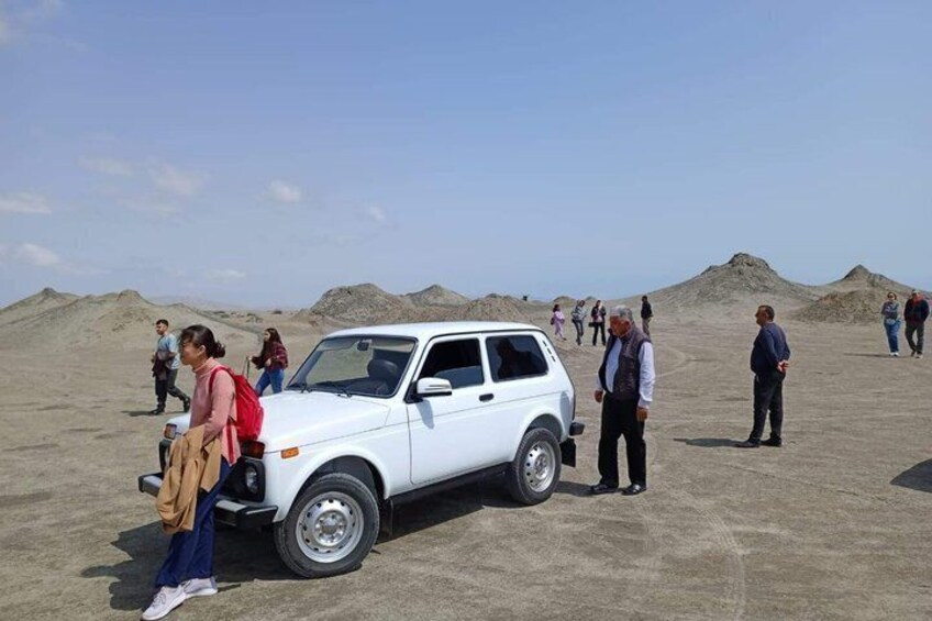 A white SUV parked on a sandy area with people walking around. 5