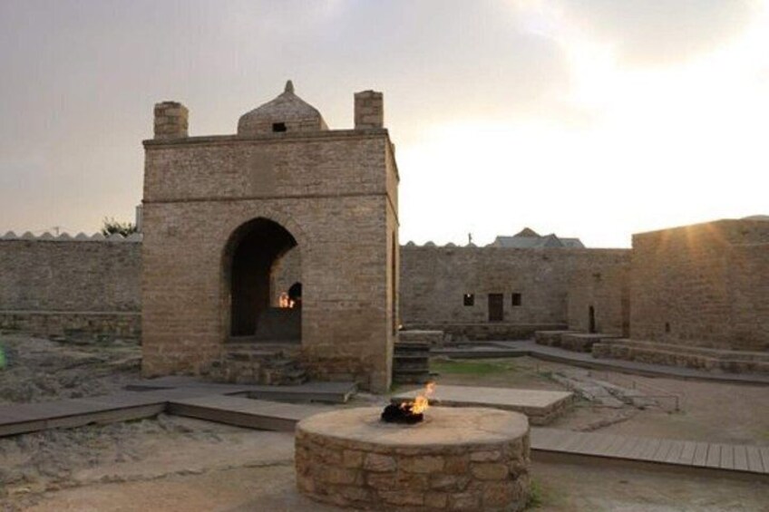 A stone building with an arched entrance, a circular stone structure with a fire, and a wall in the background. 3