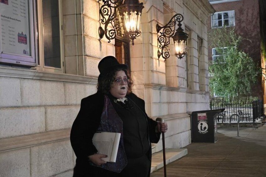 A person standing on a sidewalk next to a building with ornate street lamps and a trash bin. 2