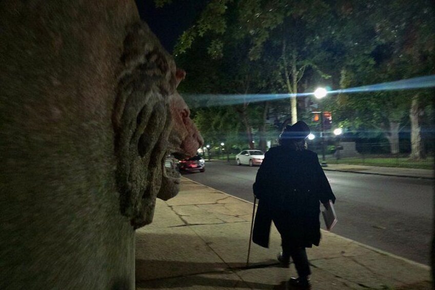 A nighttime street scene with a person walking on the sidewalk, a car driving on the road, and trees lining the street. 4