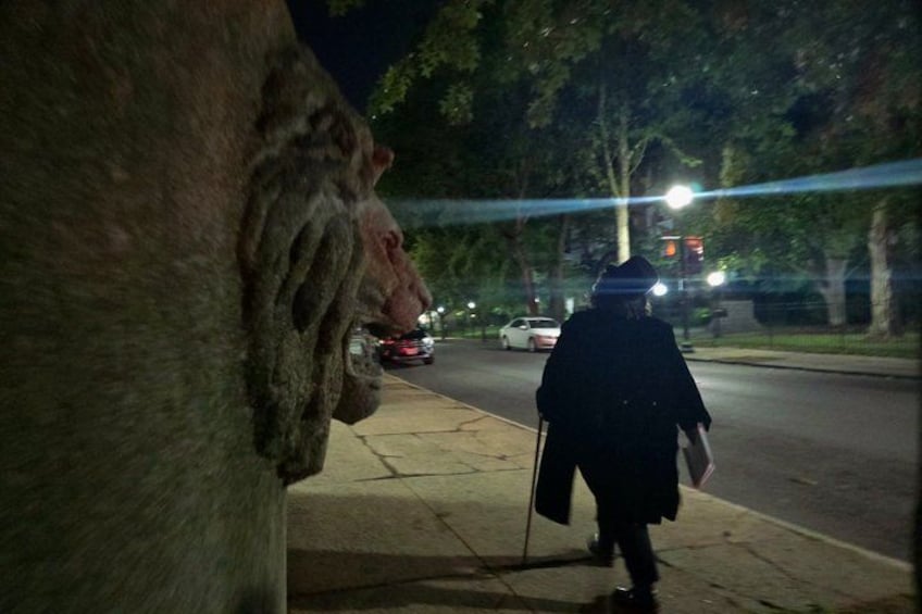 A nighttime street scene with a statue of a lion's head, a person walking with a cane, and cars on the road. 3