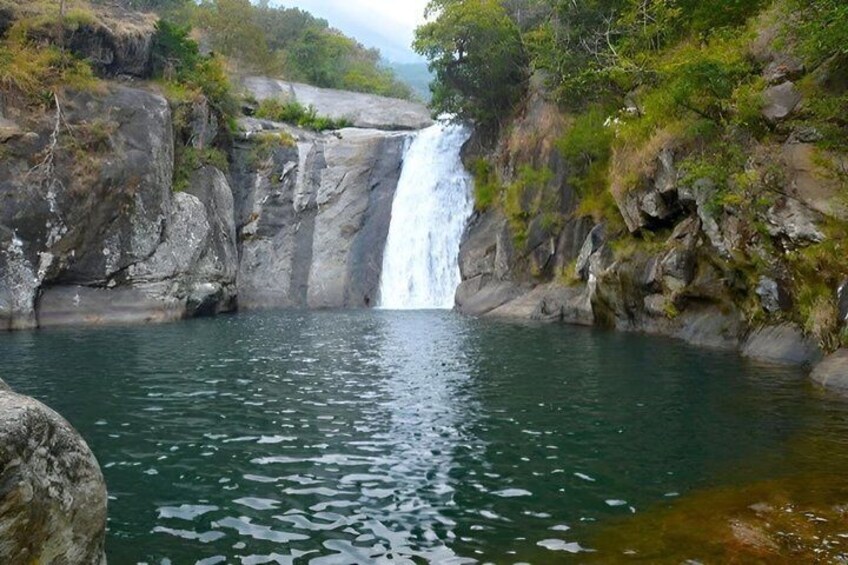 A waterfall cascading into a clear pool surrounded by rocky cliffs and greenery. 2