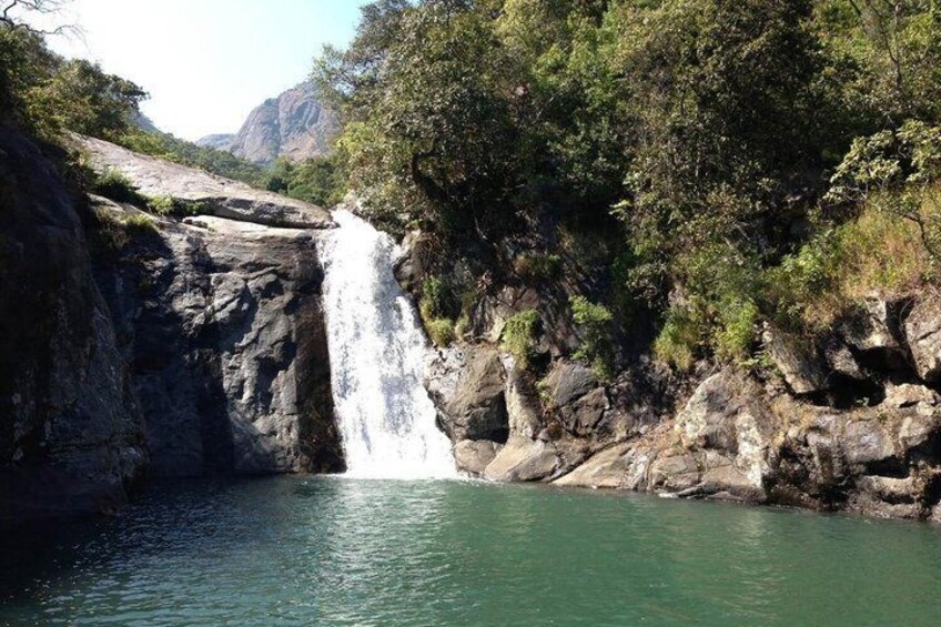 A waterfall cascading into a calm river surrounded by rocky cliffs and dense greenery. 3