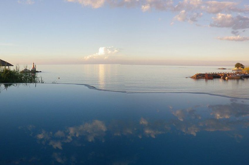 A calm sea with a clear horizon, a small island with a lighthouse, and a pier extending into the water. 2