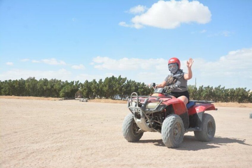 A person riding a red ATV on a sandy terrain with trees in the background. 2
