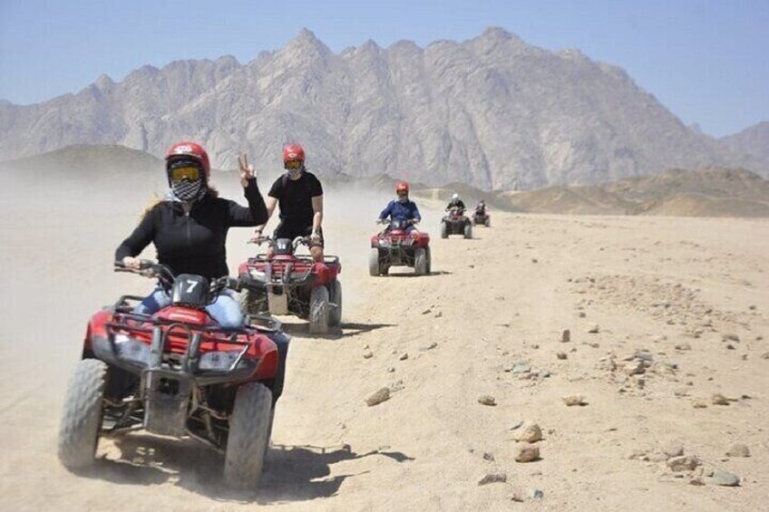 A group of people riding ATVs on a desert trail with rocky mountains in the background. 3
