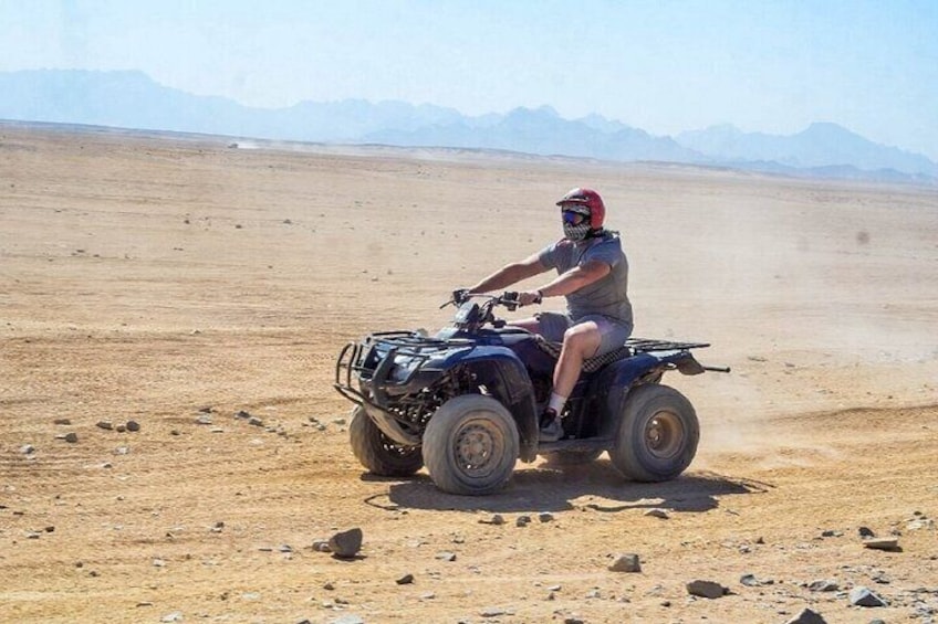 A person riding an ATV in a desert landscape with mountains in the background. 2