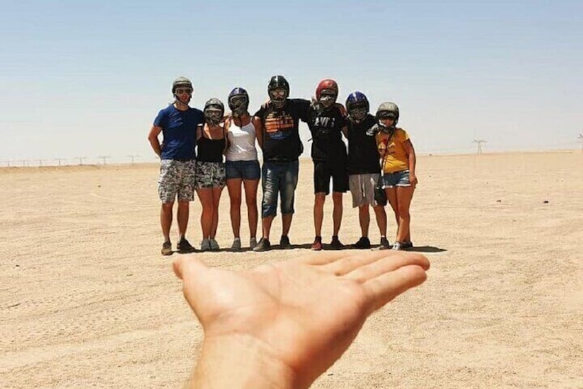 A group of people standing on a sandy beach with a hand in the foreground. 4
