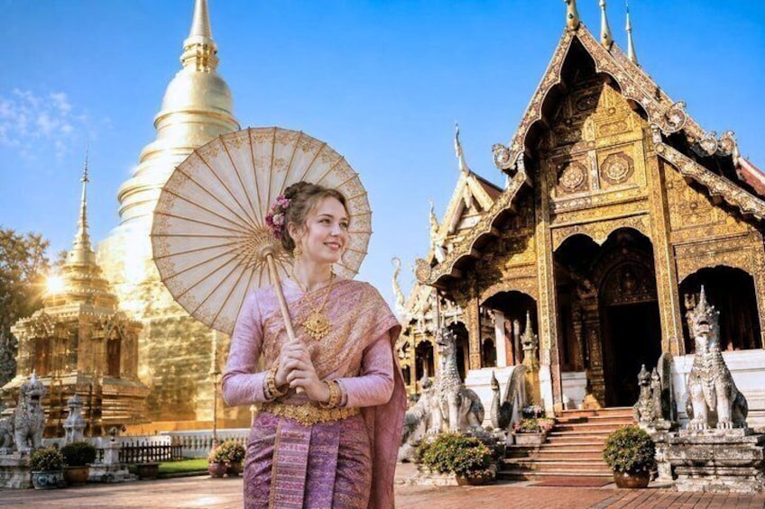 A person in traditional attire holding an umbrella, standing in front of a temple with ornate architecture. 1