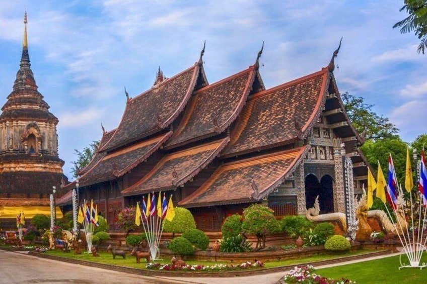 A traditional Thai temple with a multi-tiered roof, surrounded by well-maintained gardens and various flags. 5