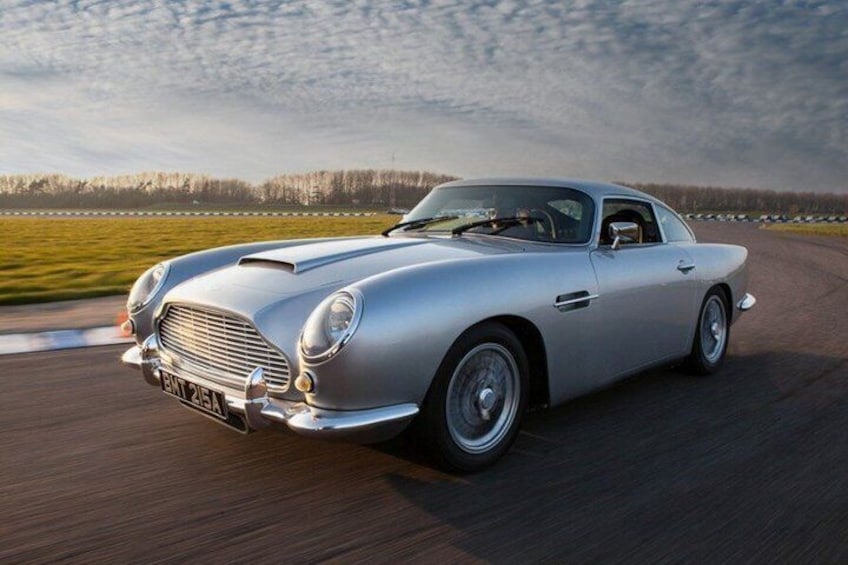 A silver classic car driving on a racetrack. 1