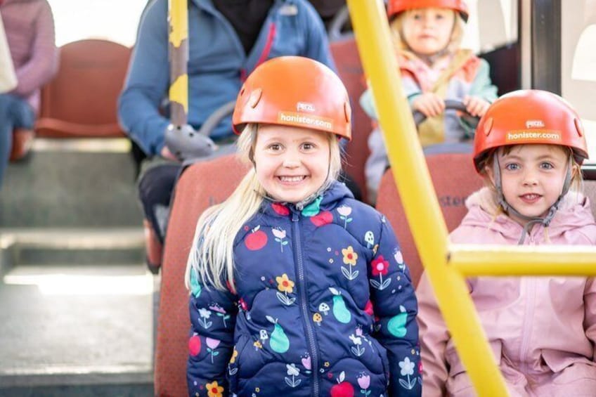 Children wearing helmets and colorful jackets seated on a bus. 1