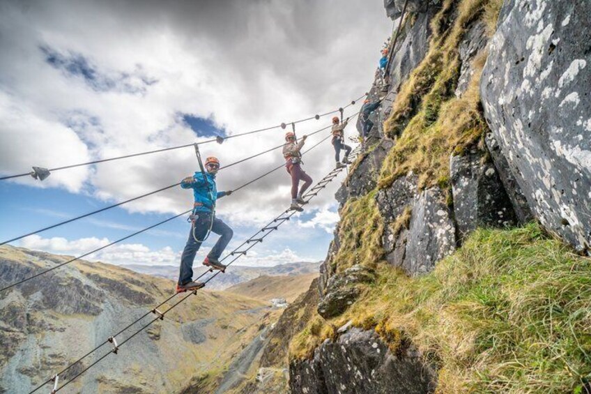 People walking on a rope bridge over a mountainous landscape. 5