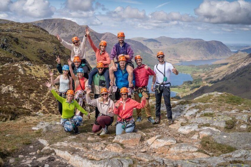 A group of people on a mountain with helmets, some climbing gear, and a lake in the background. 2