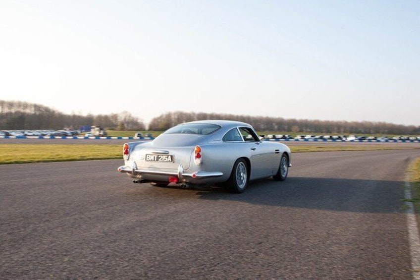 A silver car with the license plate 'BMW 215A' driving on a racetrack. 4