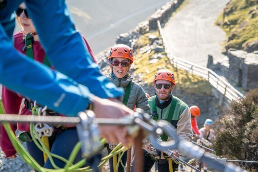 A group of people on a zip line, wearing helmets and harnesses, with a coastal landscape in the background. 2