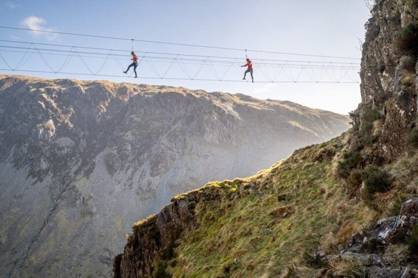 Two people walking on a suspension bridge over a steep cliff. 5
