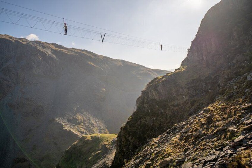A mountain landscape with a suspension bridge and a person crossing it. 4