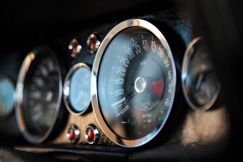 A car's speedometer and tachometer with visible RPM markings and a red needle. 2