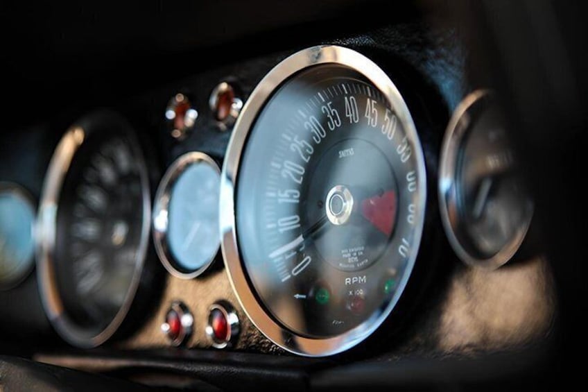 A car's speedometer and tachometer with visible RPM markings and a red needle. 2