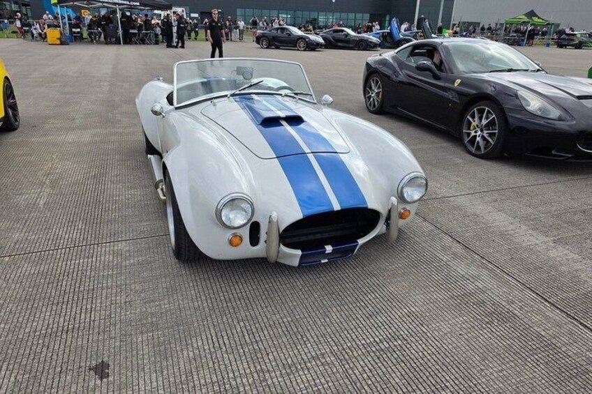 A classic sports car with a blue stripe parked on a concrete surface. 3