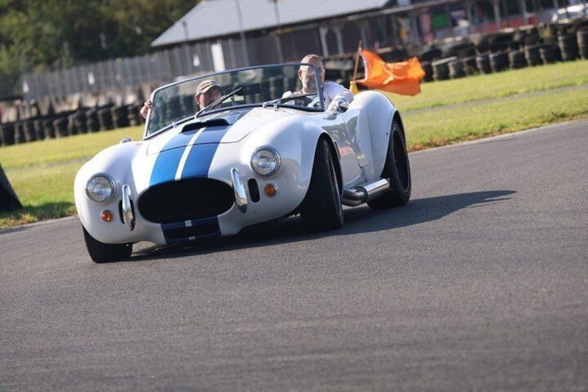 A white sports car with blue stripes driving on a track. 2