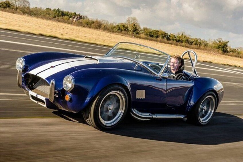 A classic blue convertible car driving on a racetrack. 1