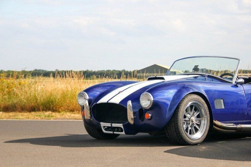 A blue convertible sports car with white racing stripes parked on a road. 4