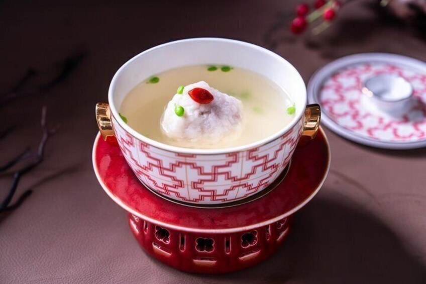 A bowl of soup with a dumpling and green garnish on a red patterned saucer. 2