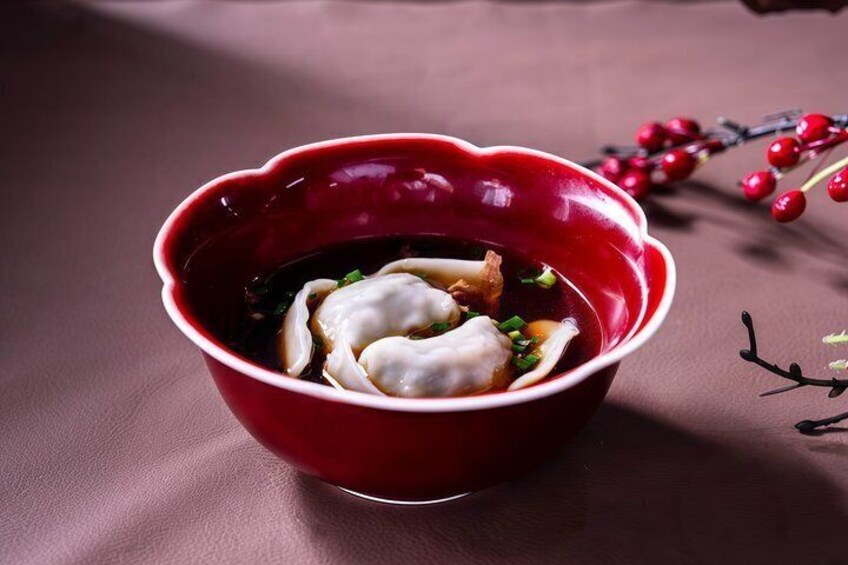 A red bowl with dumplings in a dark liquid, possibly soup, on a brown surface. 4
