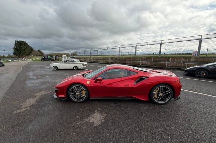 A red sports car parked in a lot with a cloudy sky and a fence in the background. 4