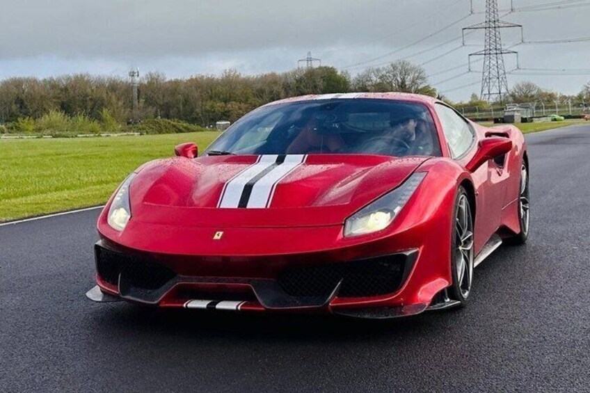 A red sports car on a road with greenery and power lines in the background. 1